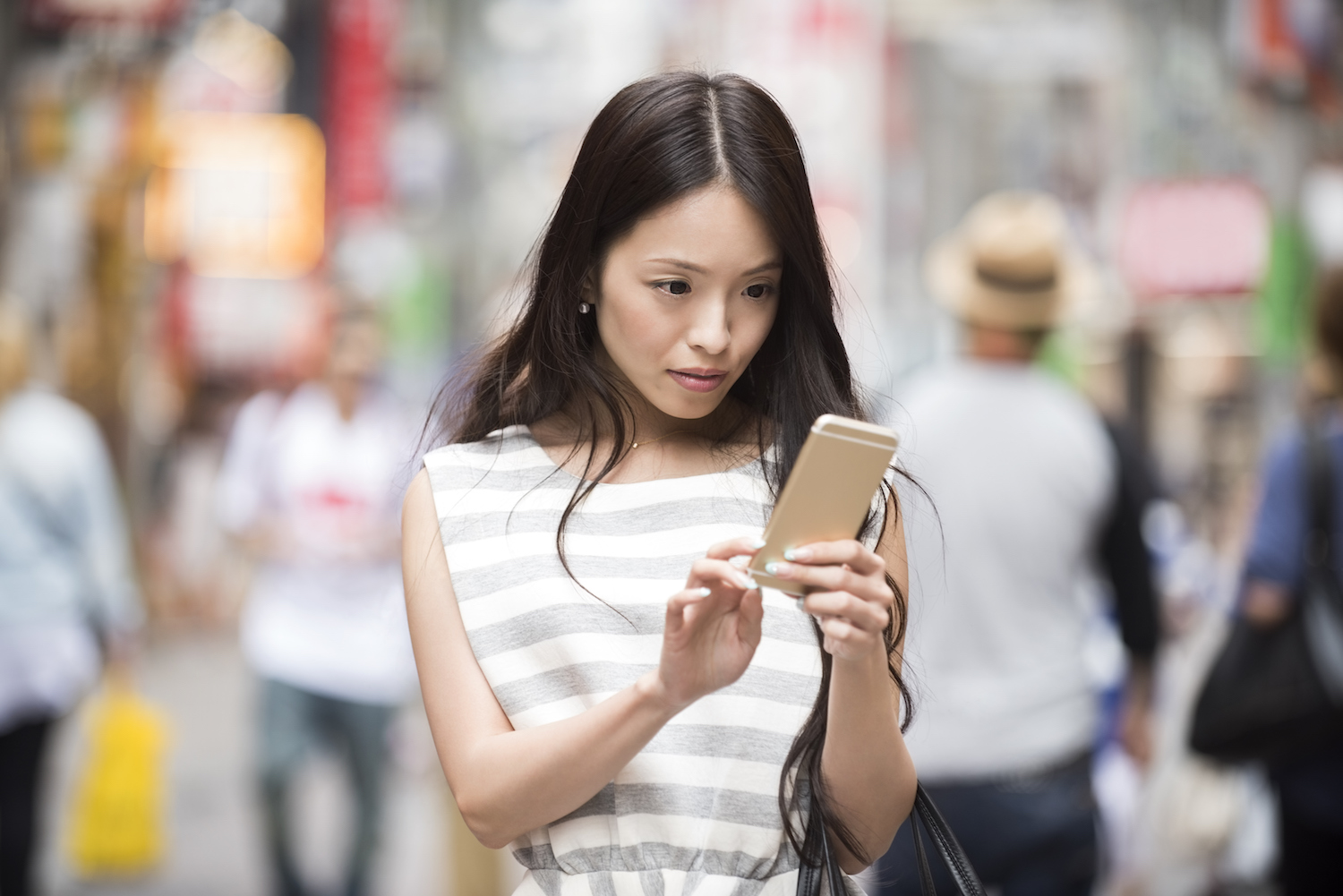 Attractive young Japanese woman using mobile phone to send text message while on the go in urban street in Shibuya, Tokyo, Japan. Asian female using smartphone outdoors.